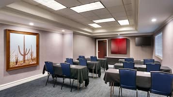 Una sala de conferencias con mesas y sillas, un cuadro en la pared, un armario rojo y un televisor montado en la pared.