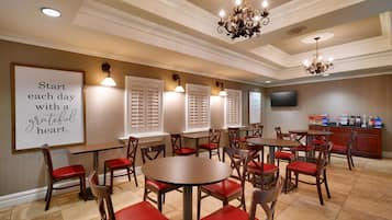 Une salle à manger d'hôtel avec des tables rondes et des chaises rembourrées de couleur rouge, un lustre et une citation inspirante affichée sur le mur.