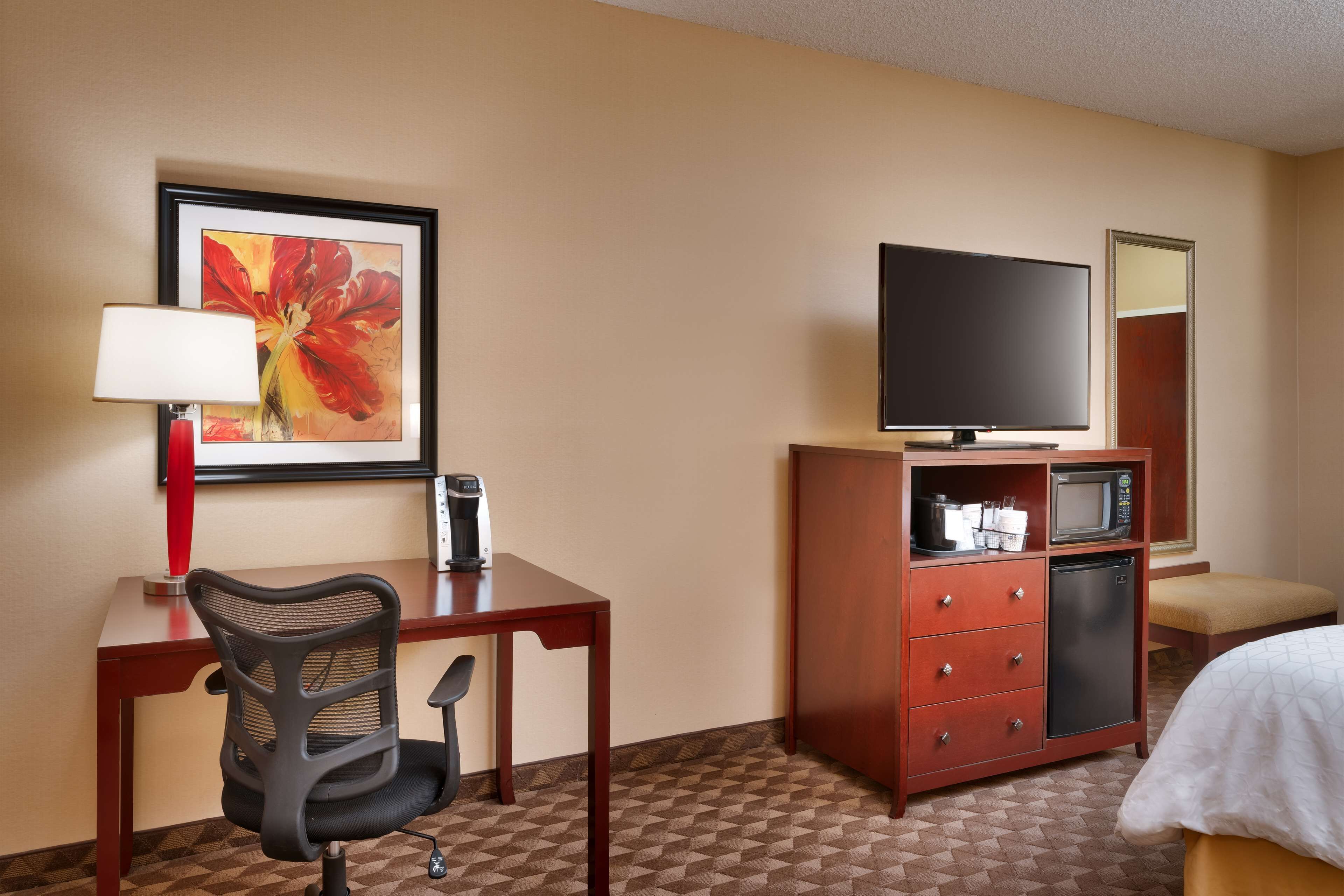 Une chambre d’hôtel équipée d’un bureau, d’une chaise, d’une télévision, d’un four à micro-ondes et d’un petit réfrigérateur.