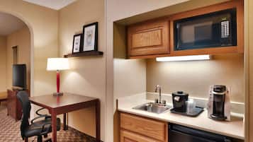 A compact hotel kitchen with a microwave, coffee maker, sink, and a small dining area with a table and chair.
