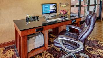 A hotel office with a desktop computer, a printer, a leather chair, and a patterned carpet.