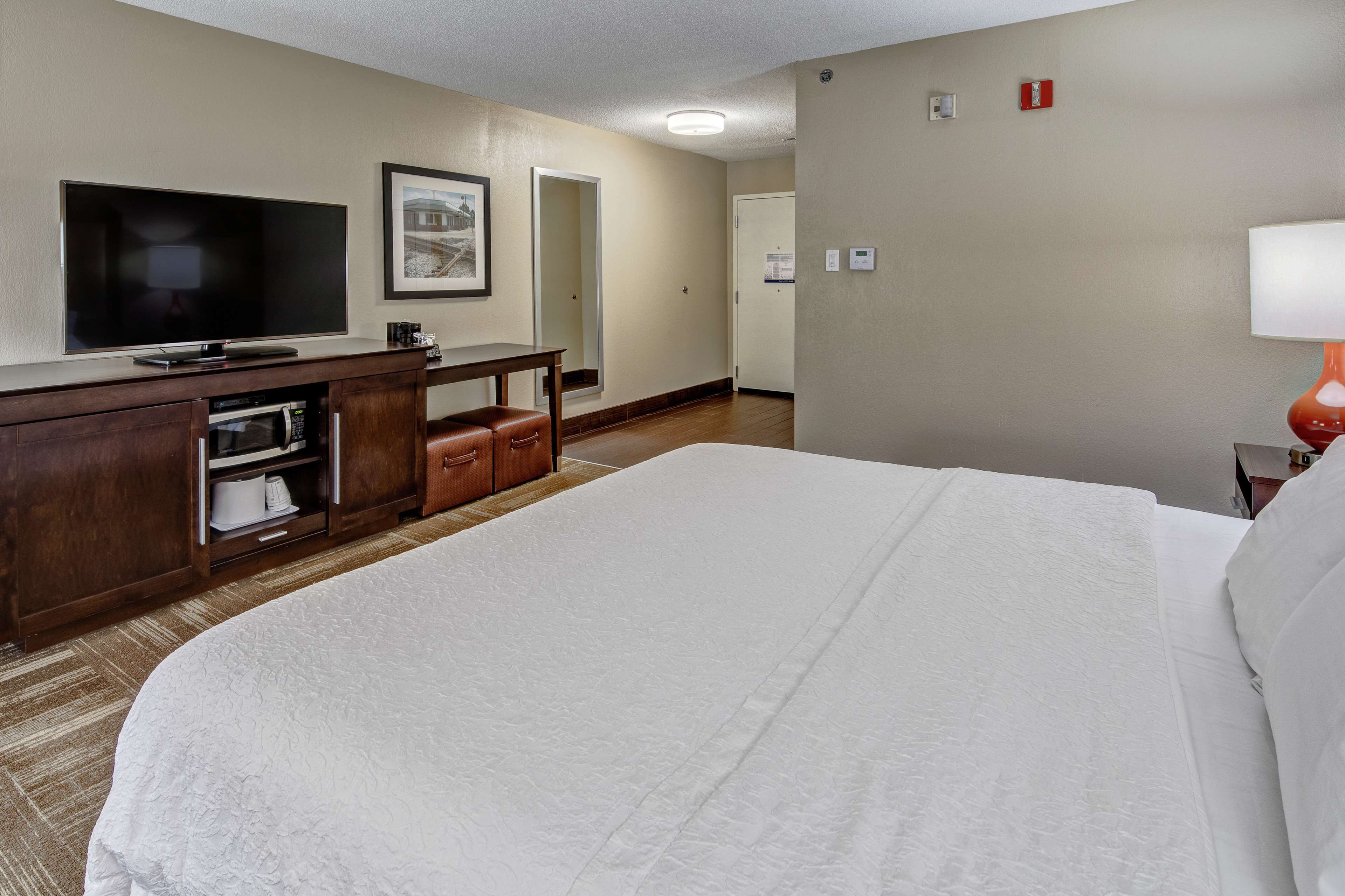 Een hotelkamer met een groot bed, een flatscreen televisie, een houten dressoir en een bureau met een lamp.