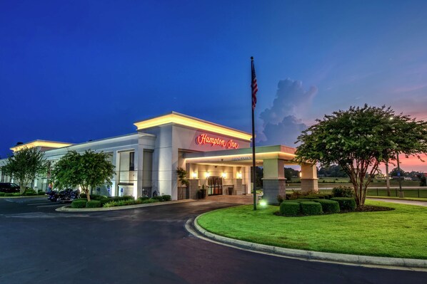 A Hampton Inn hotel with a well-lit entrance, a flagpole, and a landscaped lawn.