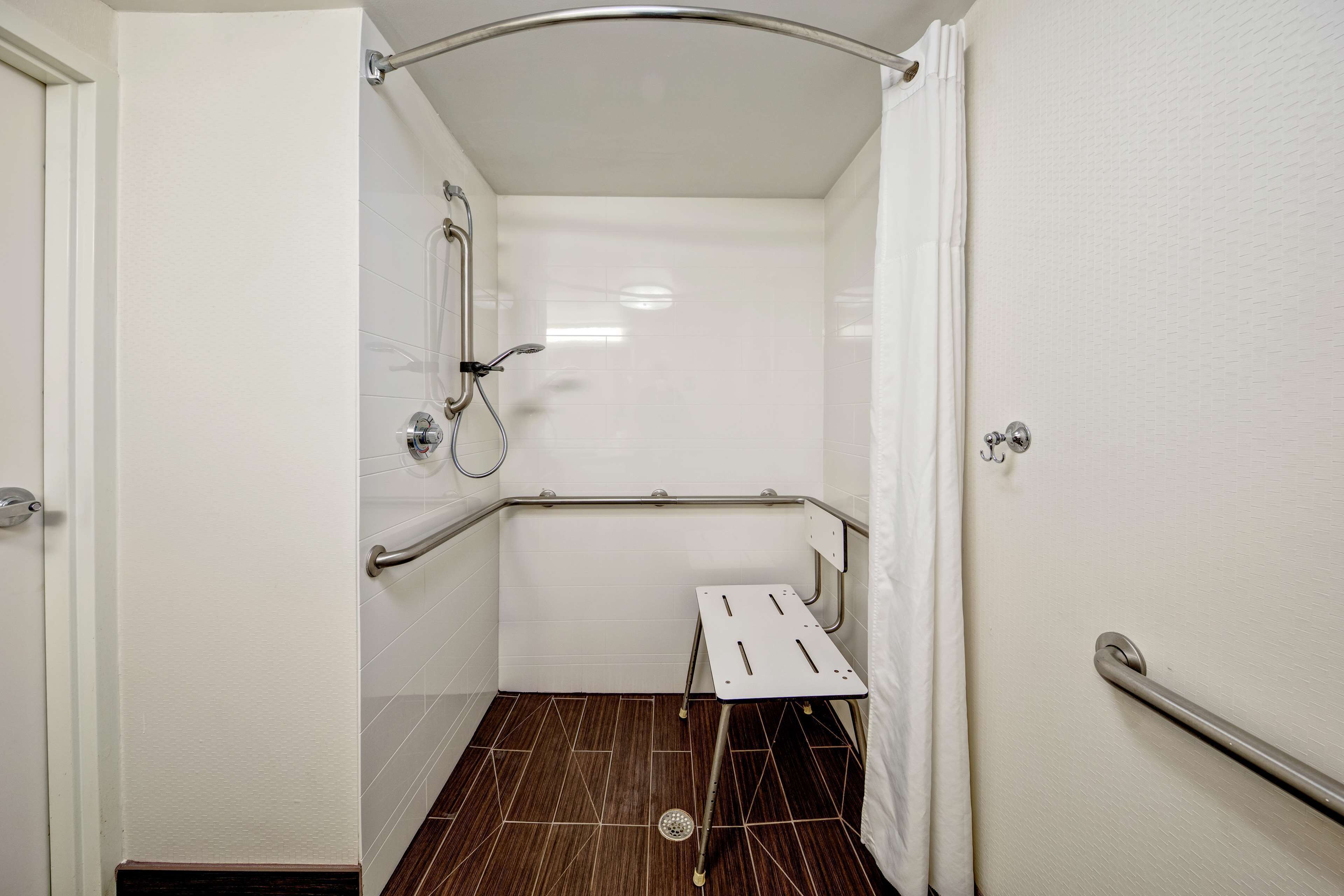 A wheelchair-accessible shower stall with a grab bar, a showerhead, and a small bench.