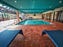 An indoor swimming pool with blue loungers, a tiled floor, and a ceiling with skylights.