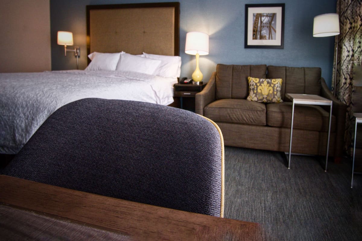 A hotel room with a large bed, a sofa, a small table, and two lamps.