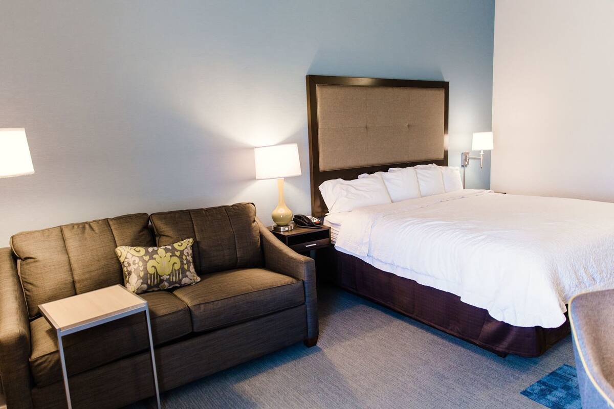 A hotel room with a bed, a sofa, a nightstand, and two bedside lamps.