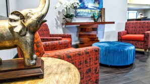 A modern interior with a large elephant sculpture on a table, red patterned sofas, a blue ottoman, and a painting on the wall. - Hampton Inn Oklahoma City/Edmond (Edmond)