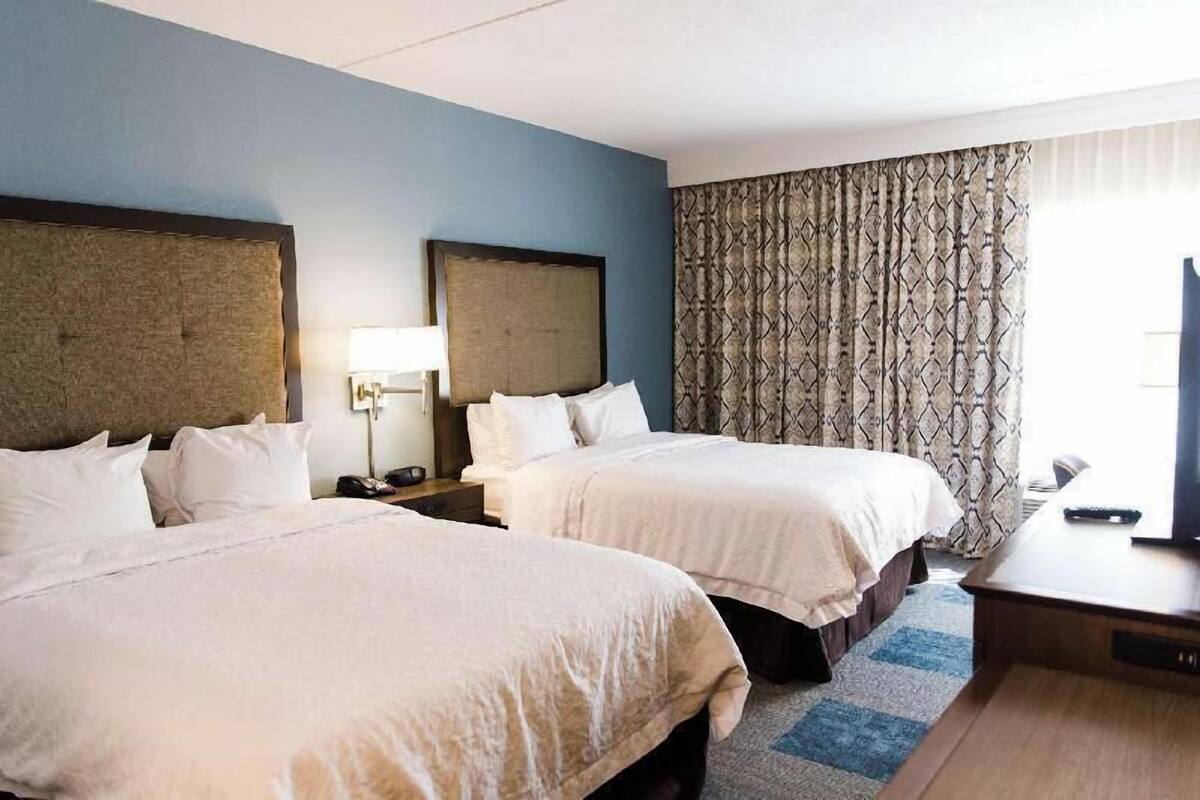 A hotel room with two beds, a desk, a lamp, and a TV.