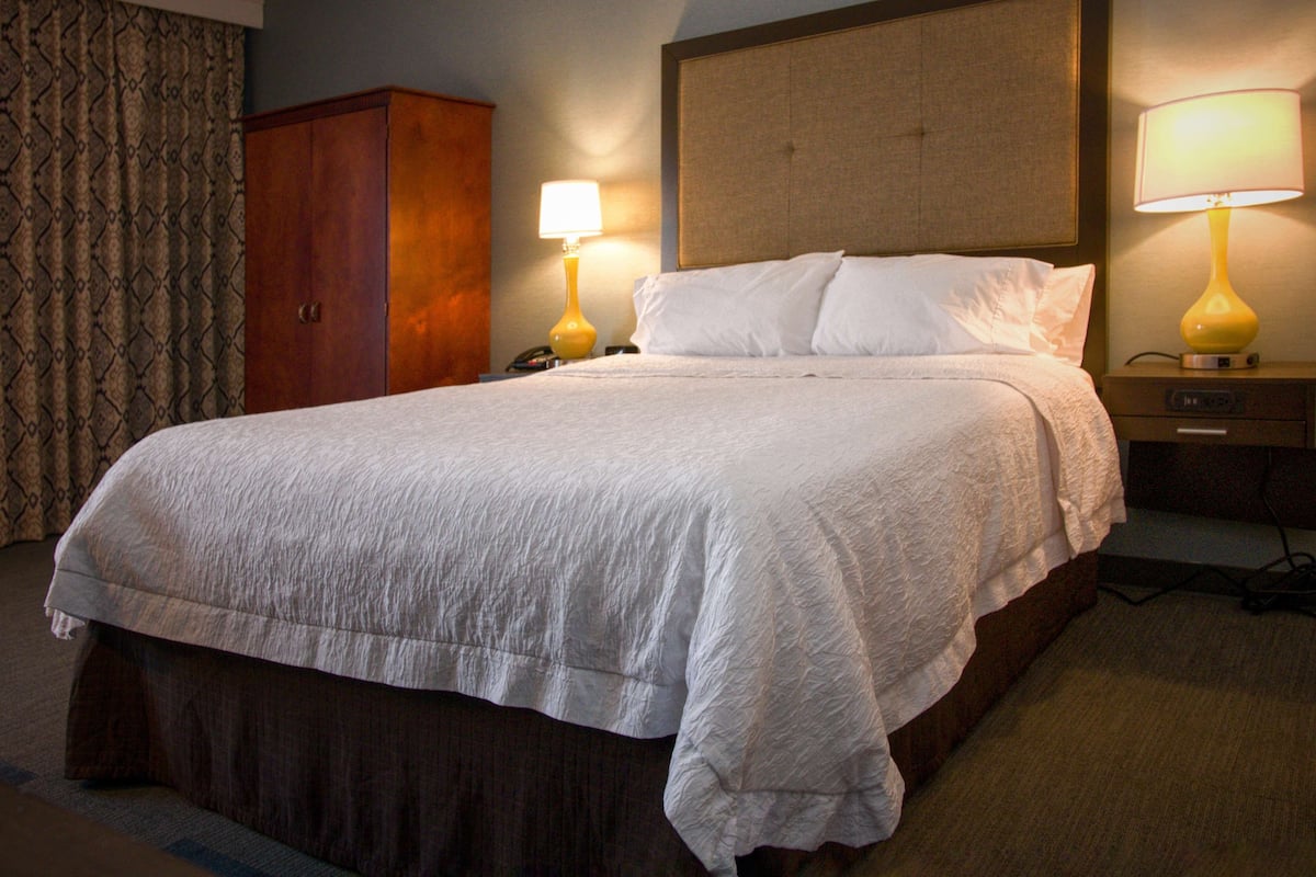 A hotel room with a large bed, two bedside lamps, a wooden wardrobe, and a headboard.