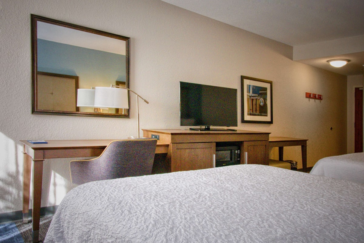 A hotel room with a bed, a desk, a chair, a television, and a mirror.
