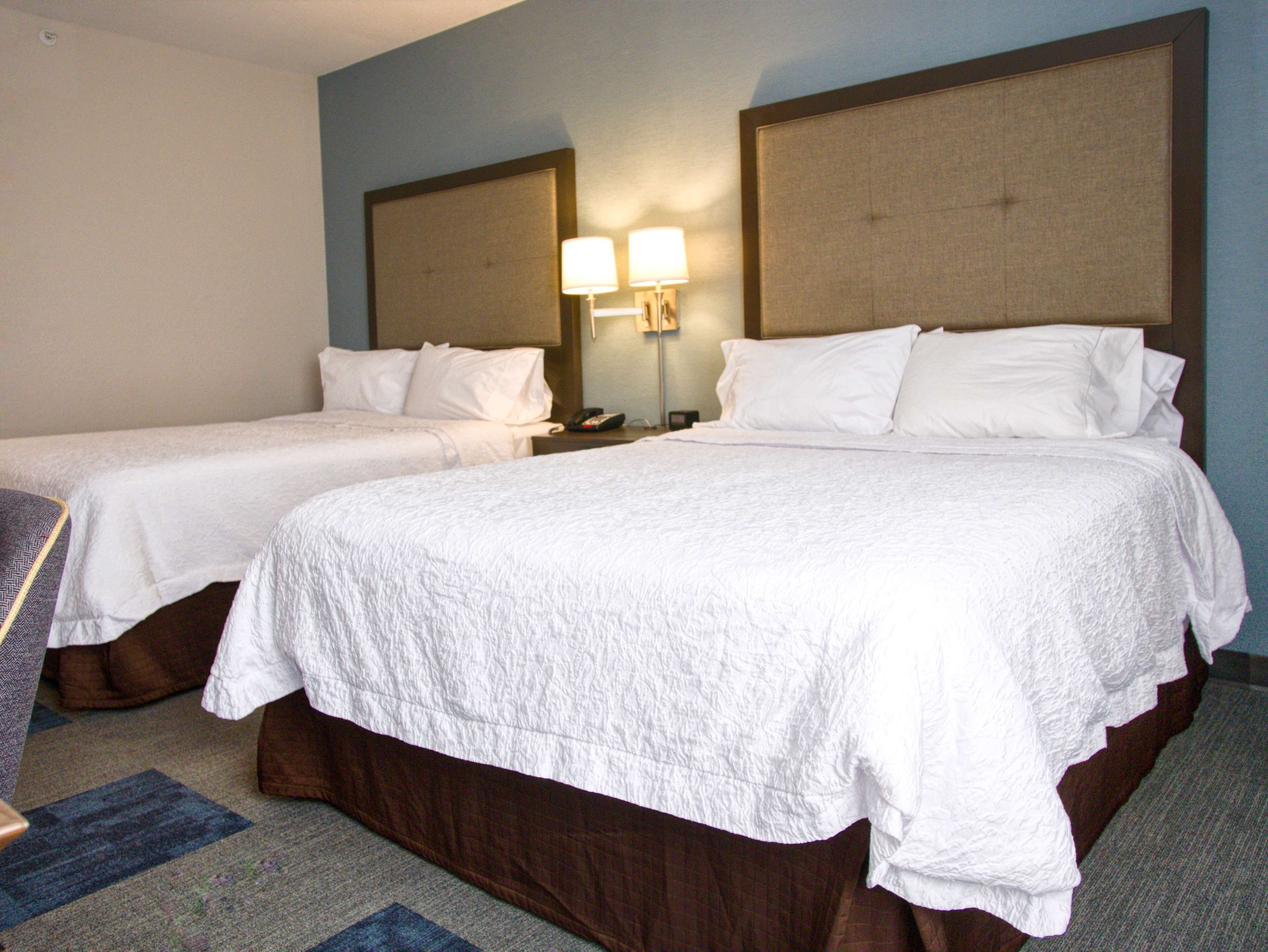 A hotel room with two single beds, a large bed, and a nightstand with a lamp.