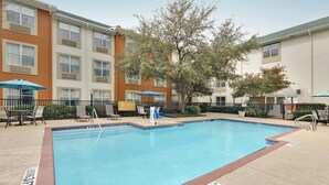 A rectangular swimming pool with a tiled edge, surrounded by lounge chairs and umbrellas, with a building in the background. - Candlewood Suites Market Center by IHG (Dallas)