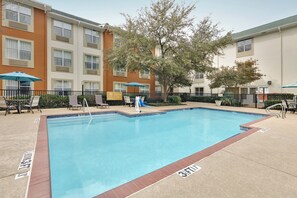 A rectangular swimming pool with a tiled edge, surrounded by lounge chairs and umbrellas, with a building in the background. - Candlewood Suites Market Center by IHG (Dallas)