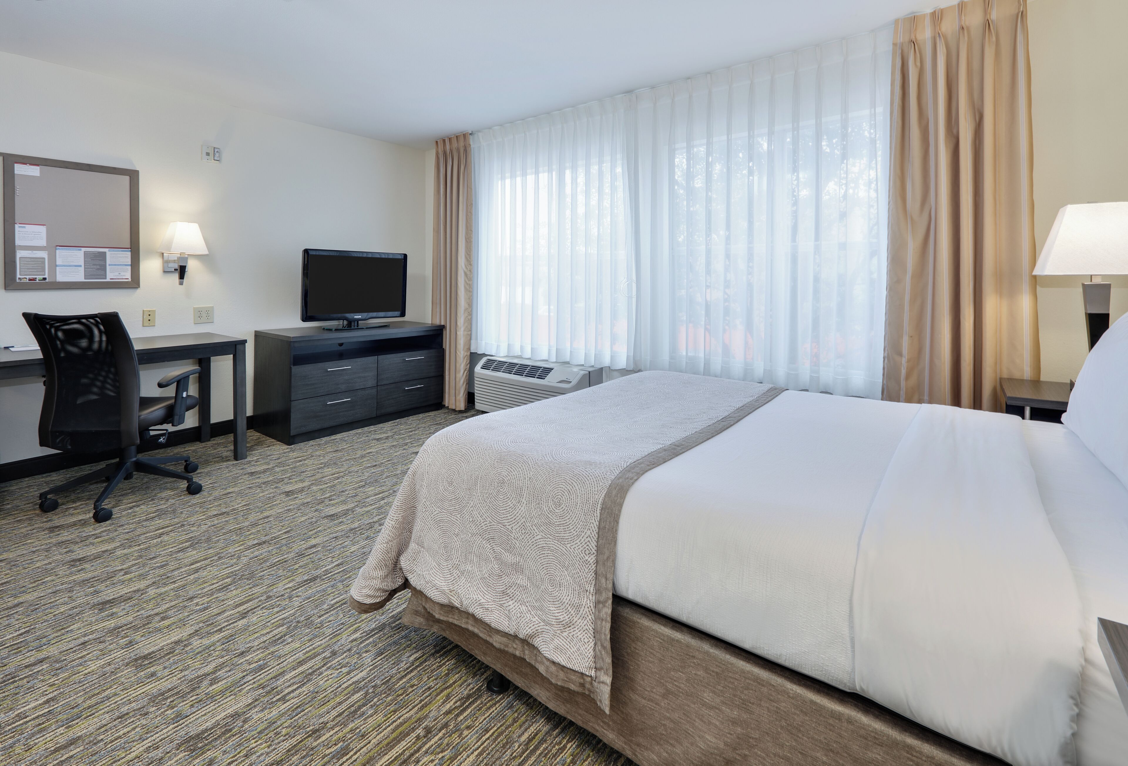 A hotel room with a bed, desk, chair, television, and a window with curtains.