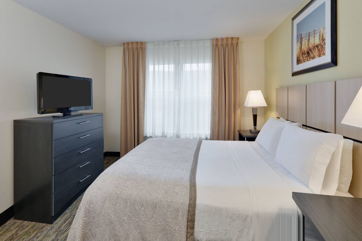 A hotel room with a bed, a TV on a dresser, a lamp, and a painting on the wall.