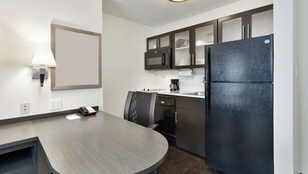 A modern kitchen with a large island, dark cabinets, and a black refrigerator. - Candlewood Suites Market Center by IHG (Dallas)
