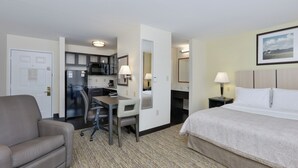 A hotel room with a bed, a desk, a chair, a kitchenette, and a door. - Candlewood Suites Market Center by IHG (Dallas)