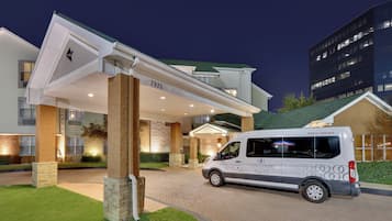 Una entrada de hotel moderna con fachada blanca, pilares de piedra y una furgoneta estacionada adelante.