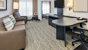 A hotel room with a sofa, a desk, a chair, a TV, and a lamp. - Candlewood Suites Market Center by IHG (Dallas)