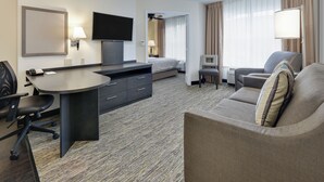 A hotel room with a bed, a desk with a chair, a sofa, and a TV. - Candlewood Suites Market Center by IHG (Dallas)