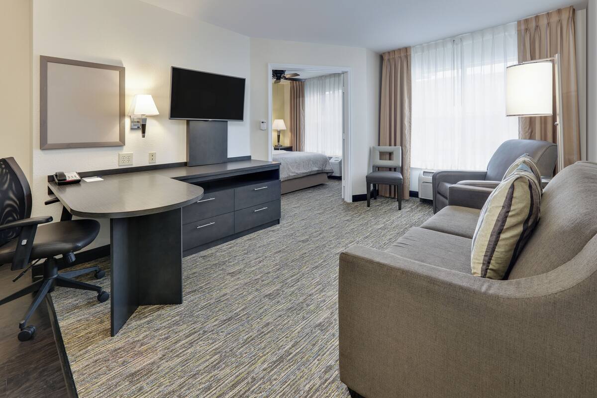 A hotel room with a bed, a desk with a chair, a sofa, and a TV.