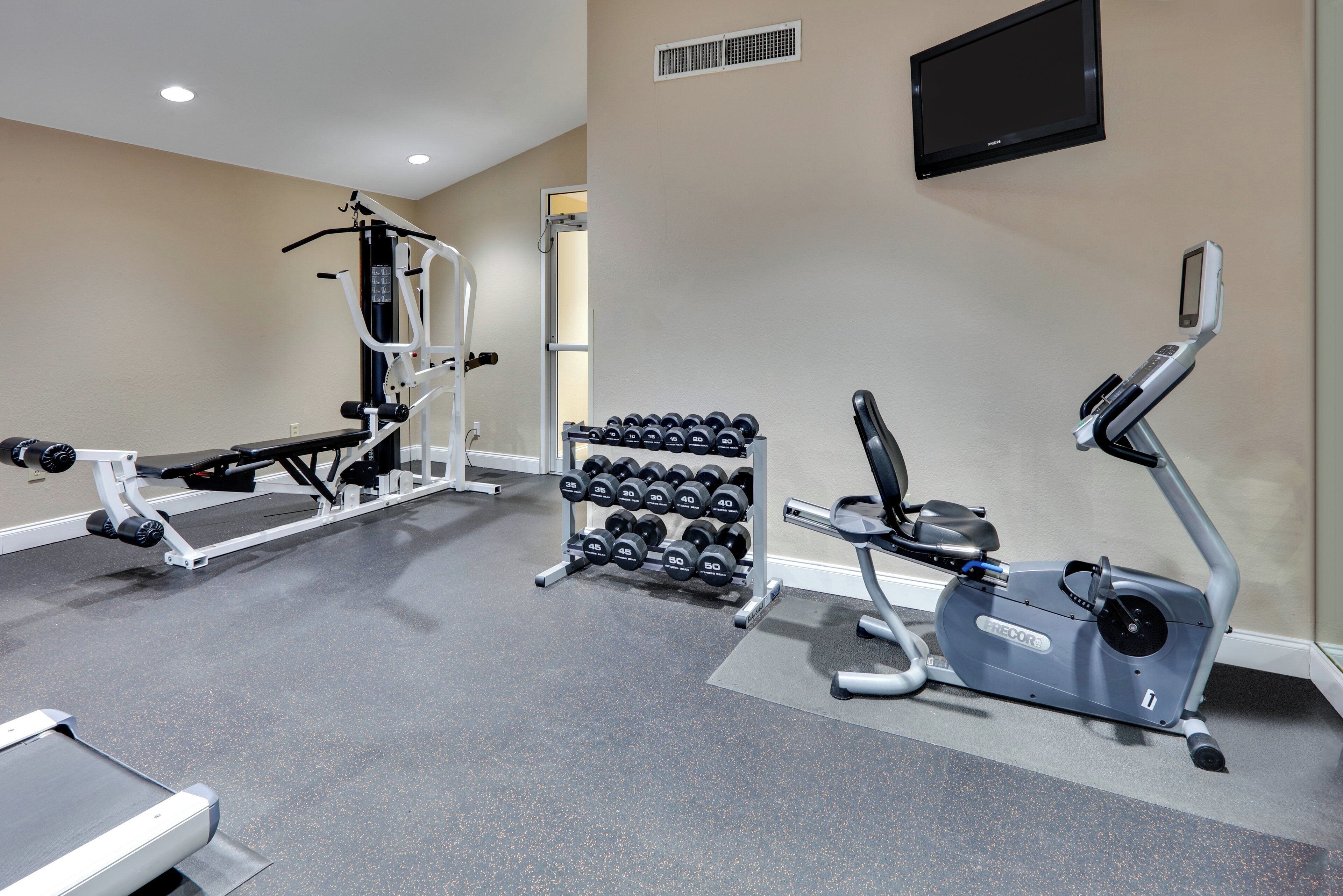 A gym with exercise equipment including a bench press, dumbbells, and an elliptical machine.