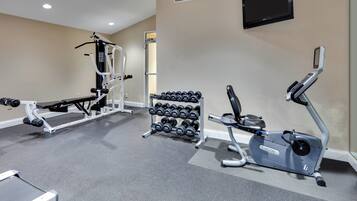 A gym with exercise equipment including a bench press, dumbbells, and an elliptical machine.