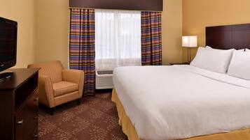 A hotel room with a large bed, a television, a chair, a desk, and a window with curtains.