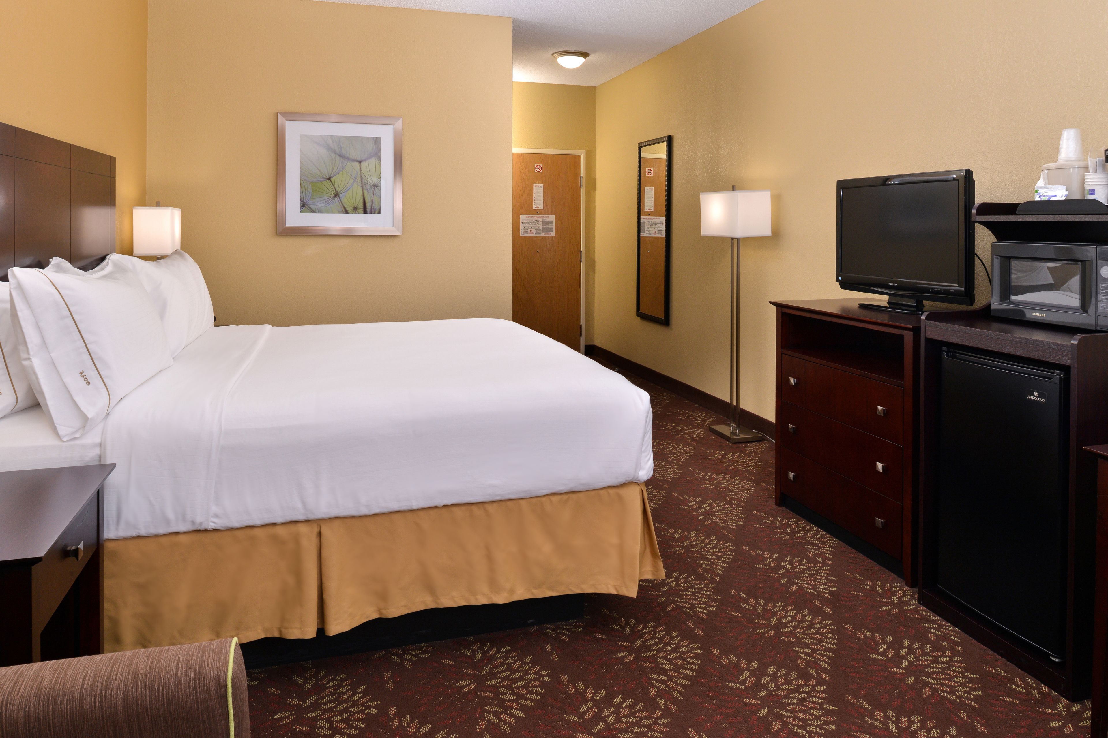 A hotel room with a large bed, a desk with a lamp, a television, and a microwave.