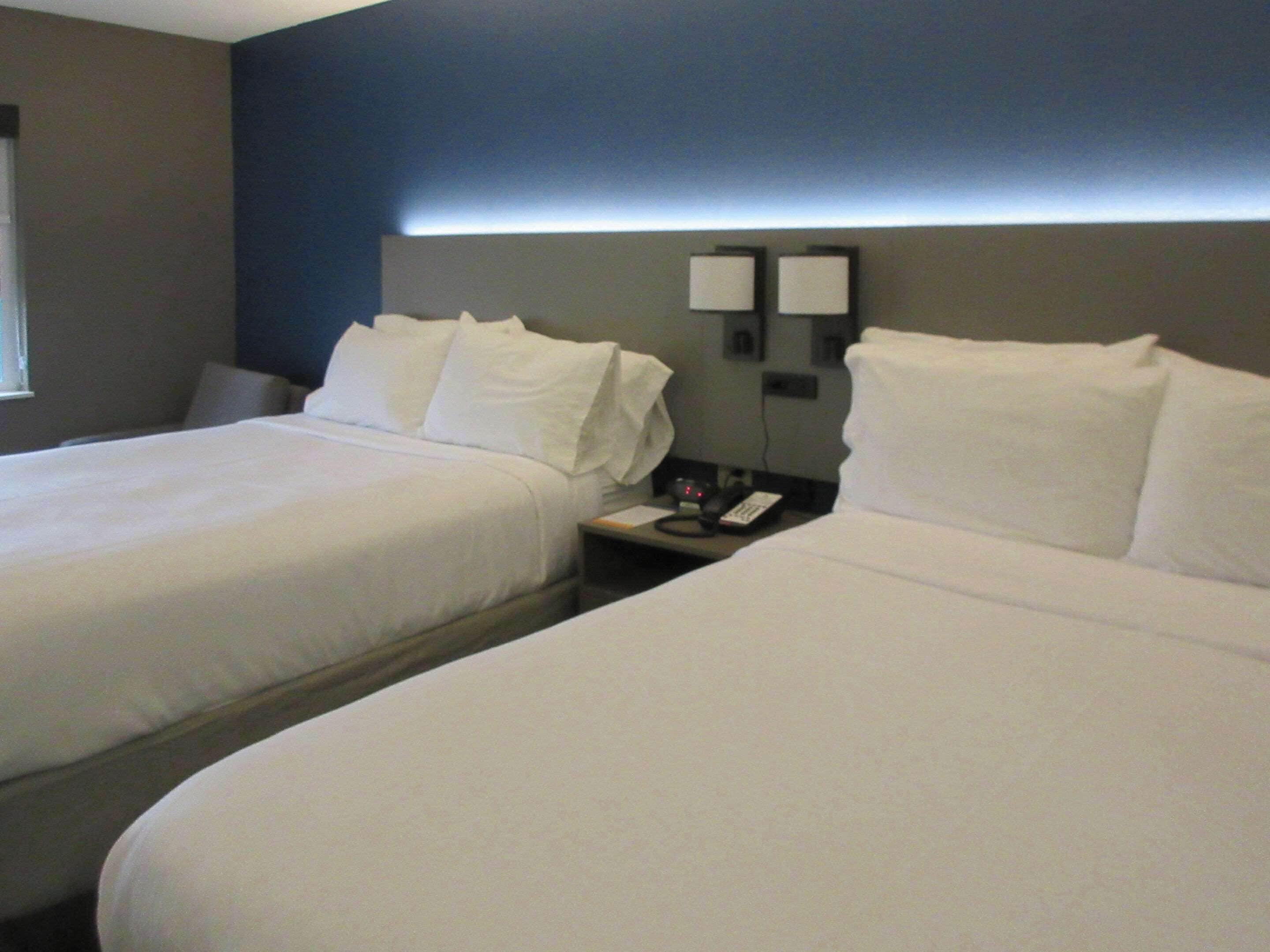 Una habitación de hotel con dos camas, una mesita de noche con teléfono y una lámpara de pared.