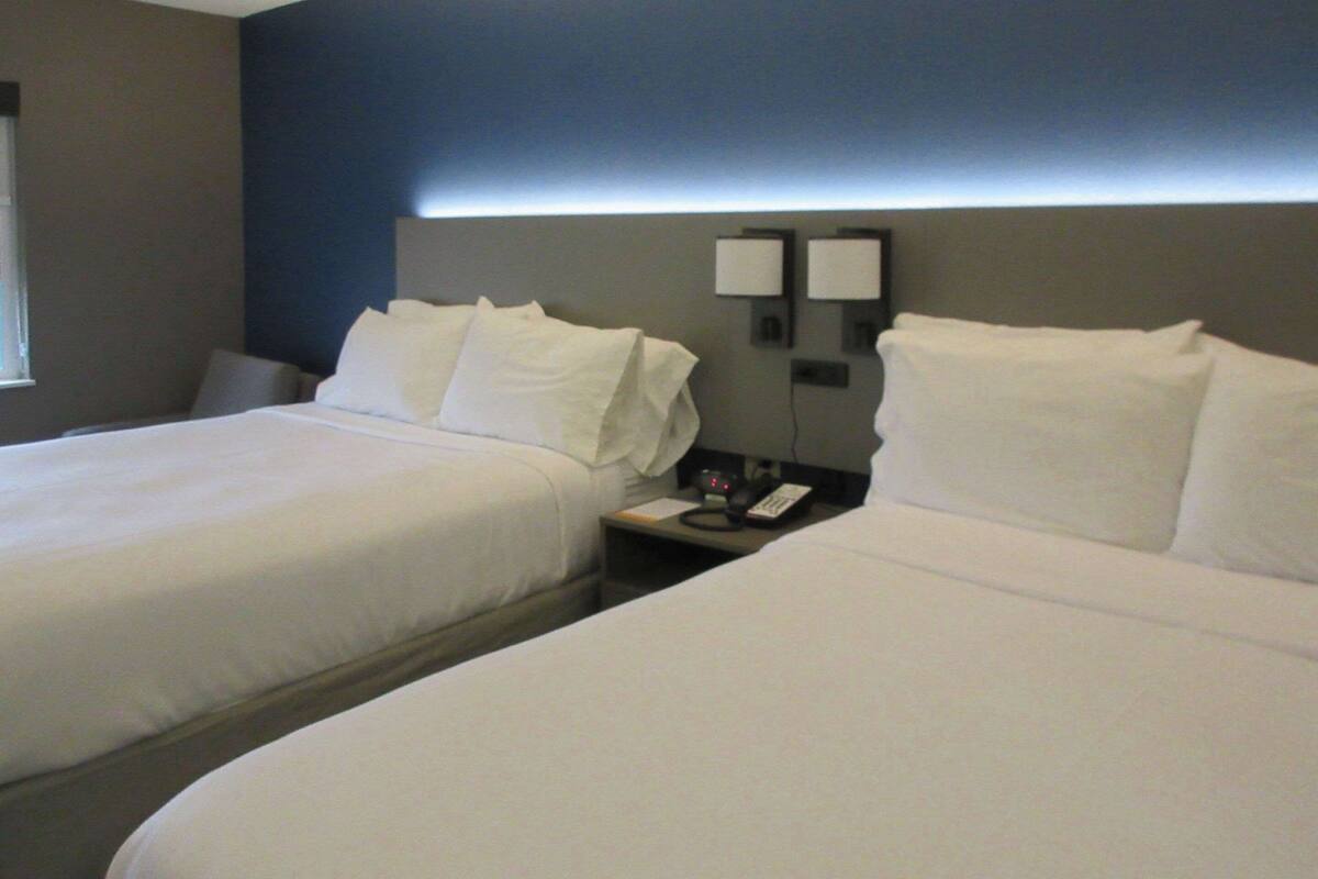 A hotel room with two beds, a nightstand with a phone, and a wall-mounted light.