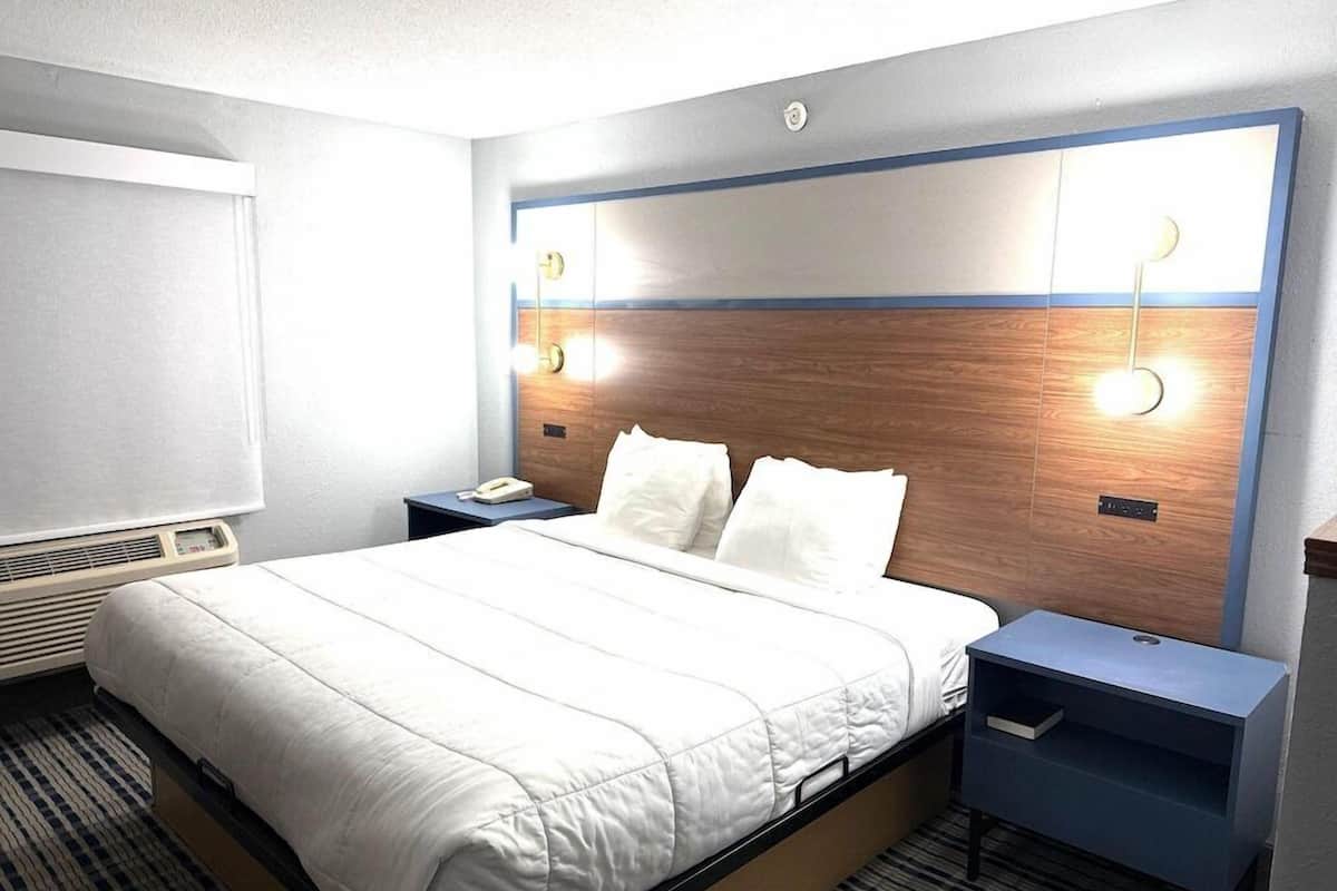 Une chambre d’hôtel comprenant un lit, des tables de chevet, une petite table, un luminaire fixé au mur et une fenêtre.