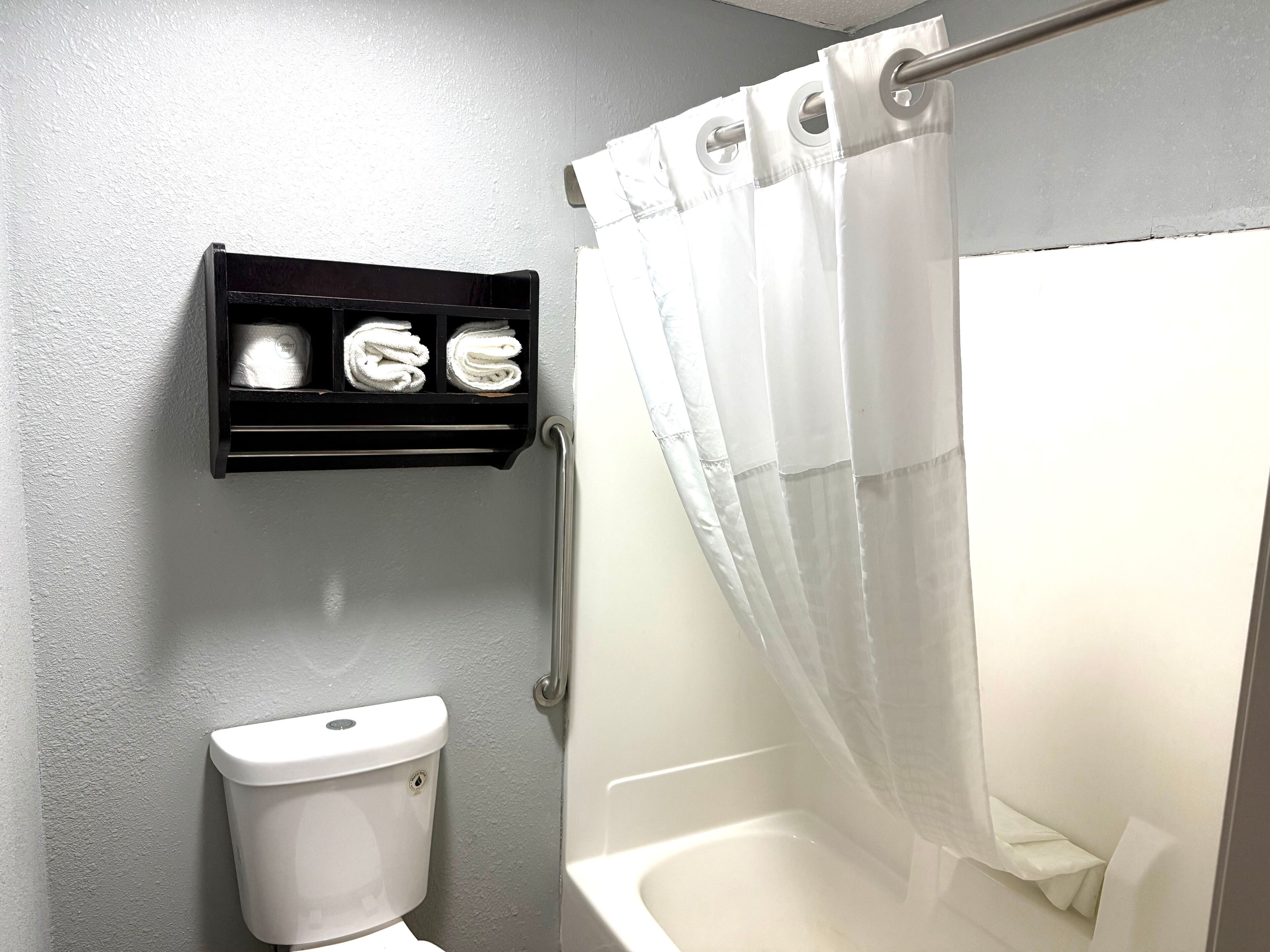 A bathroom with a toilet, a shower with a curtain, and a towel rack with towels.
