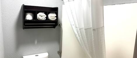 A bathroom with a toilet, a shower with a curtain, and a towel rack with towels.