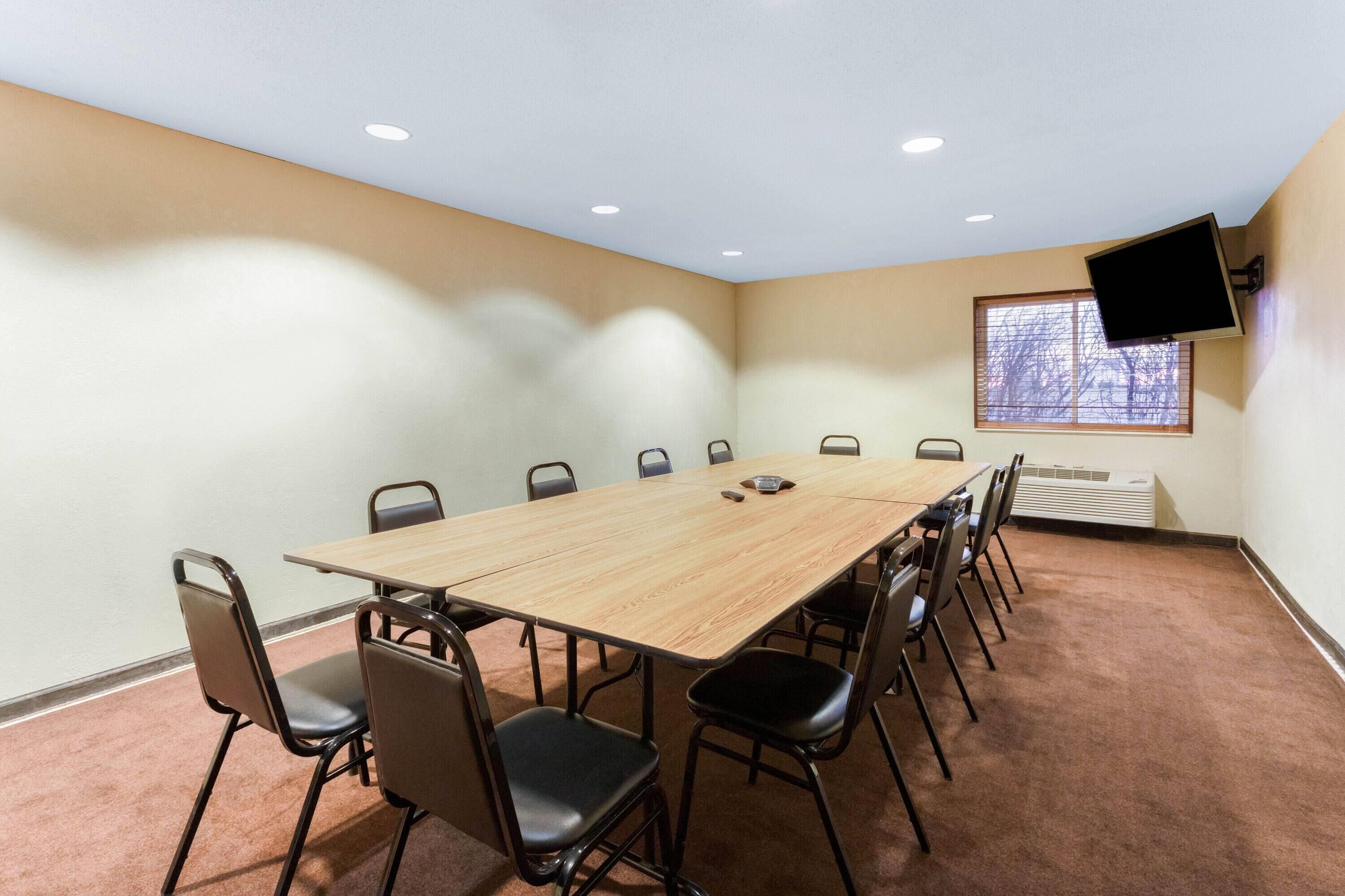 A conference room with a long table, chairs, a mounted TV, and a window with blinds.