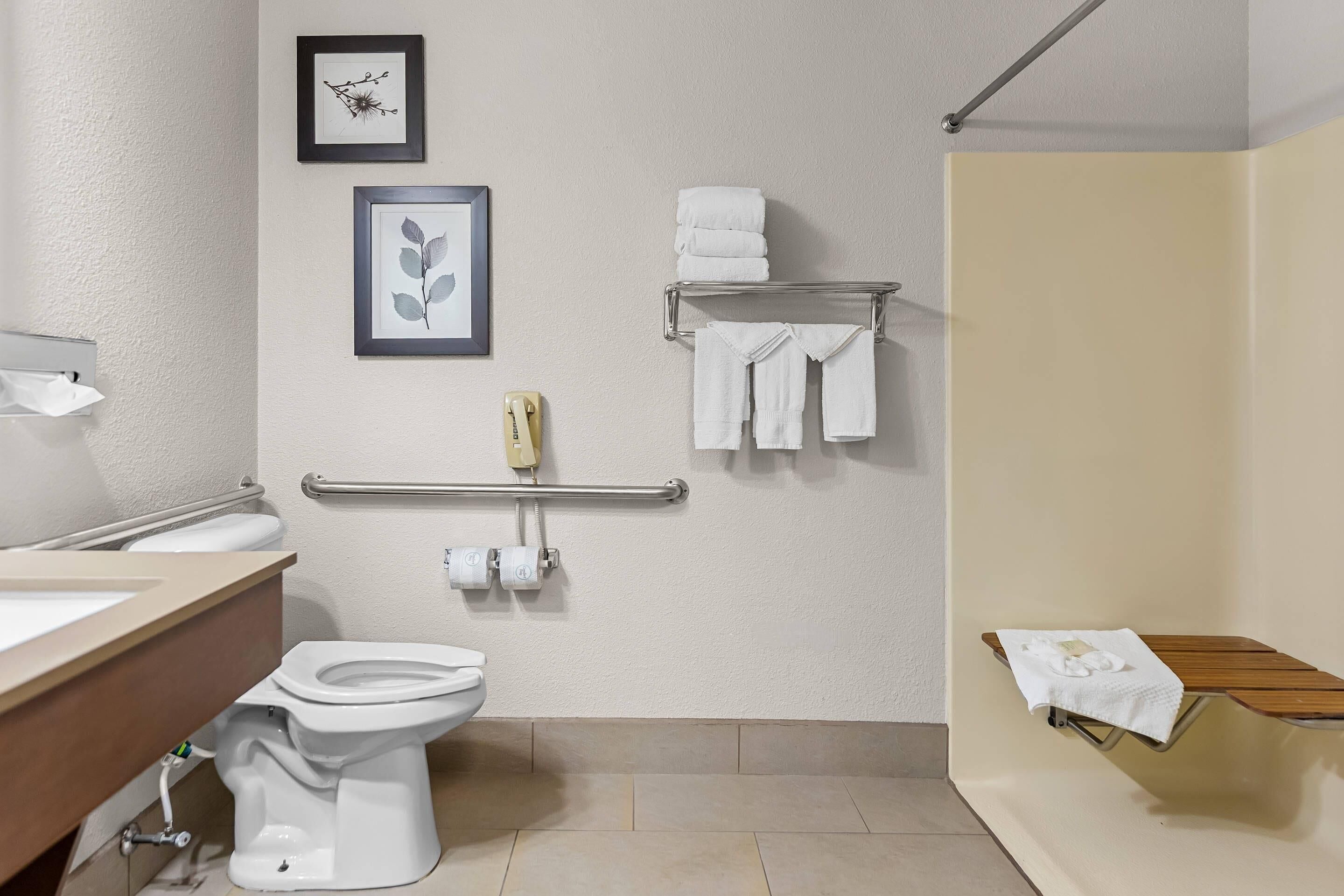 A bathroom with a toilet, sink, framed artwork, towel rack, and a bench.