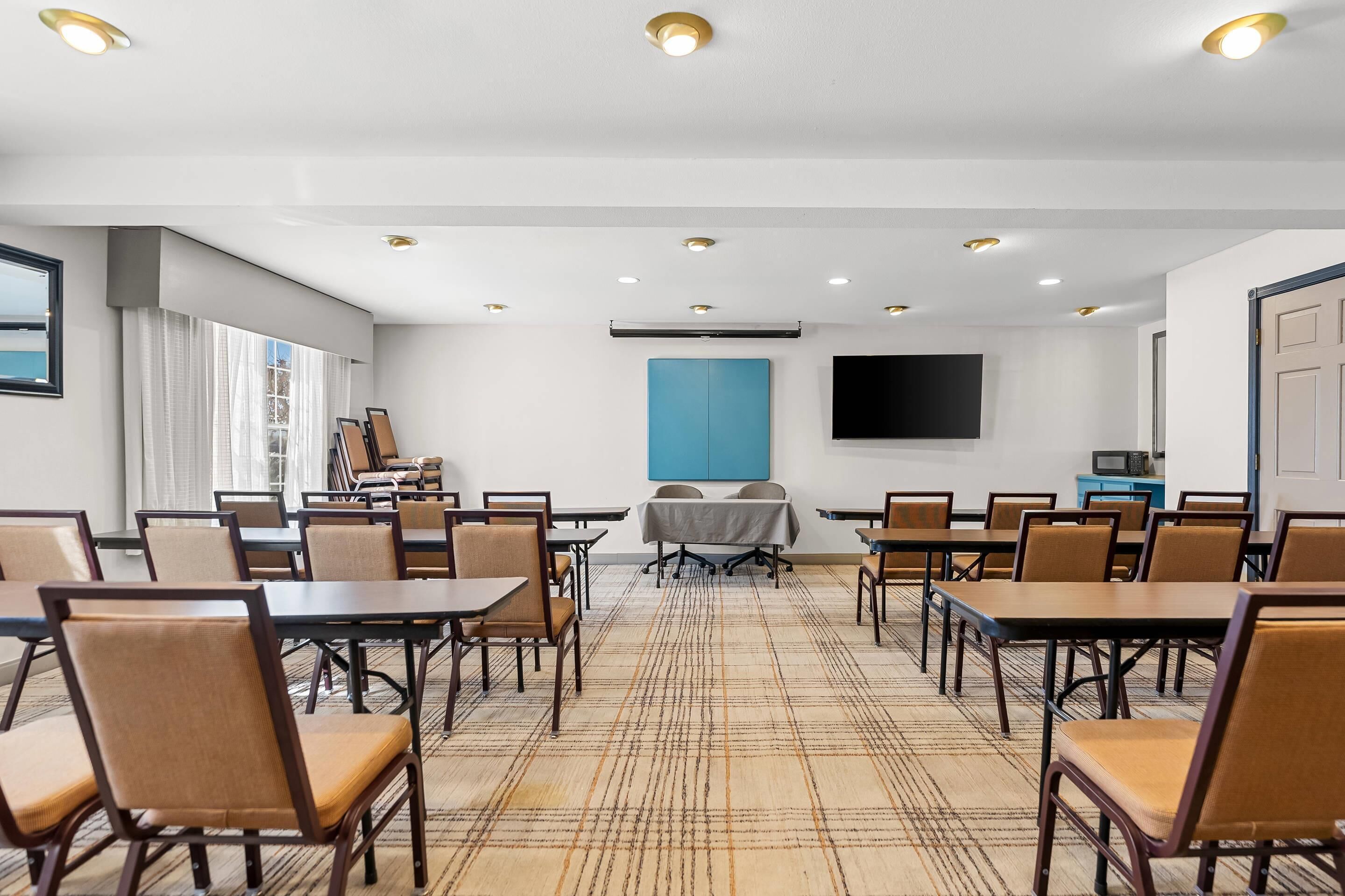 A conference room with tables and chairs, a flat-screen TV, and a large window with curtains.
