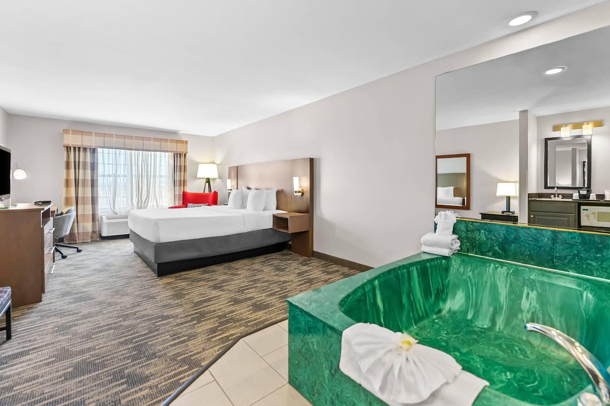 A hotel room with a bed, desk, chair, and a green marble bathtub.
