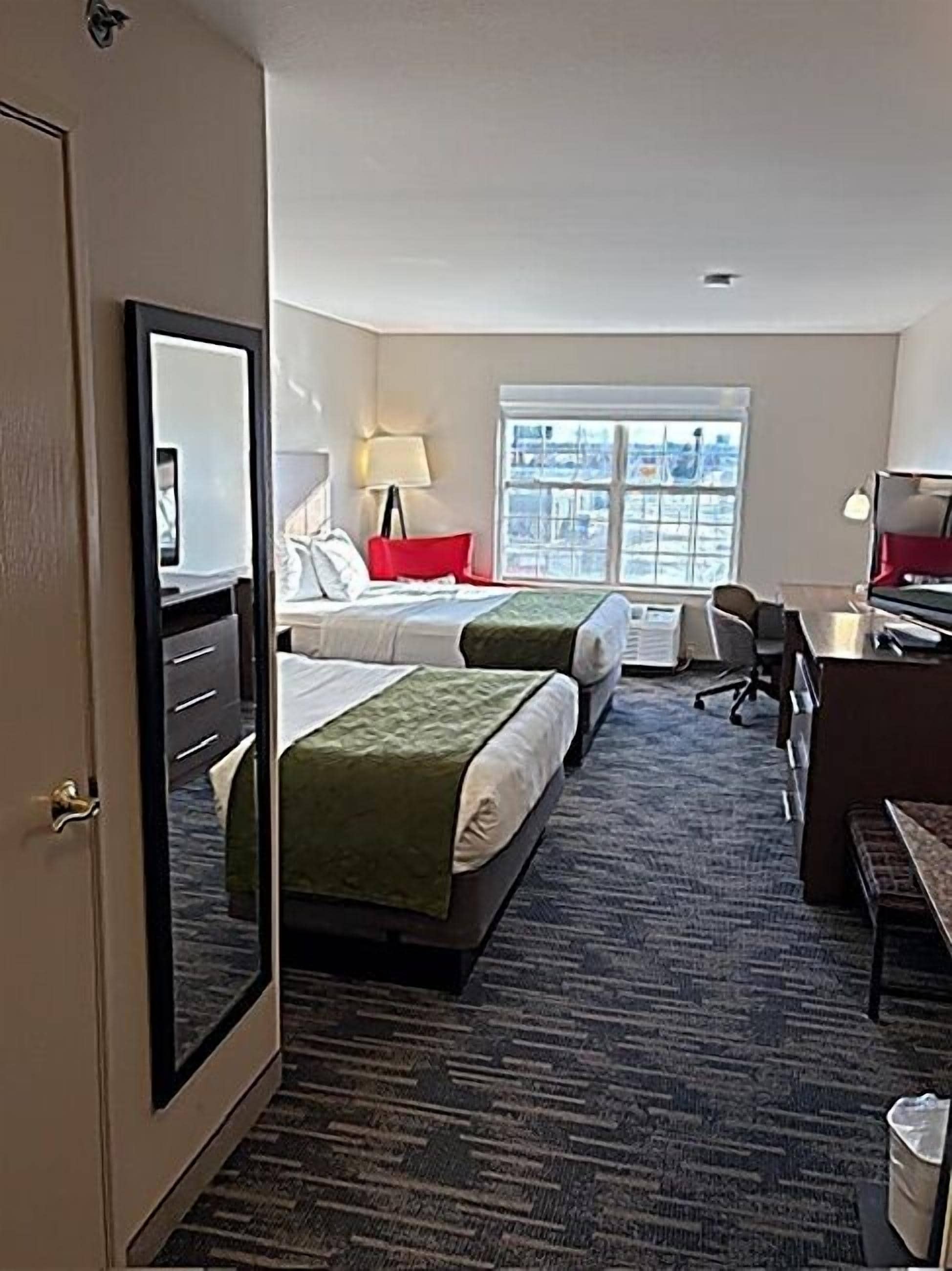 A hotel room with two beds, a desk, a chair, a lamp, and a large window.