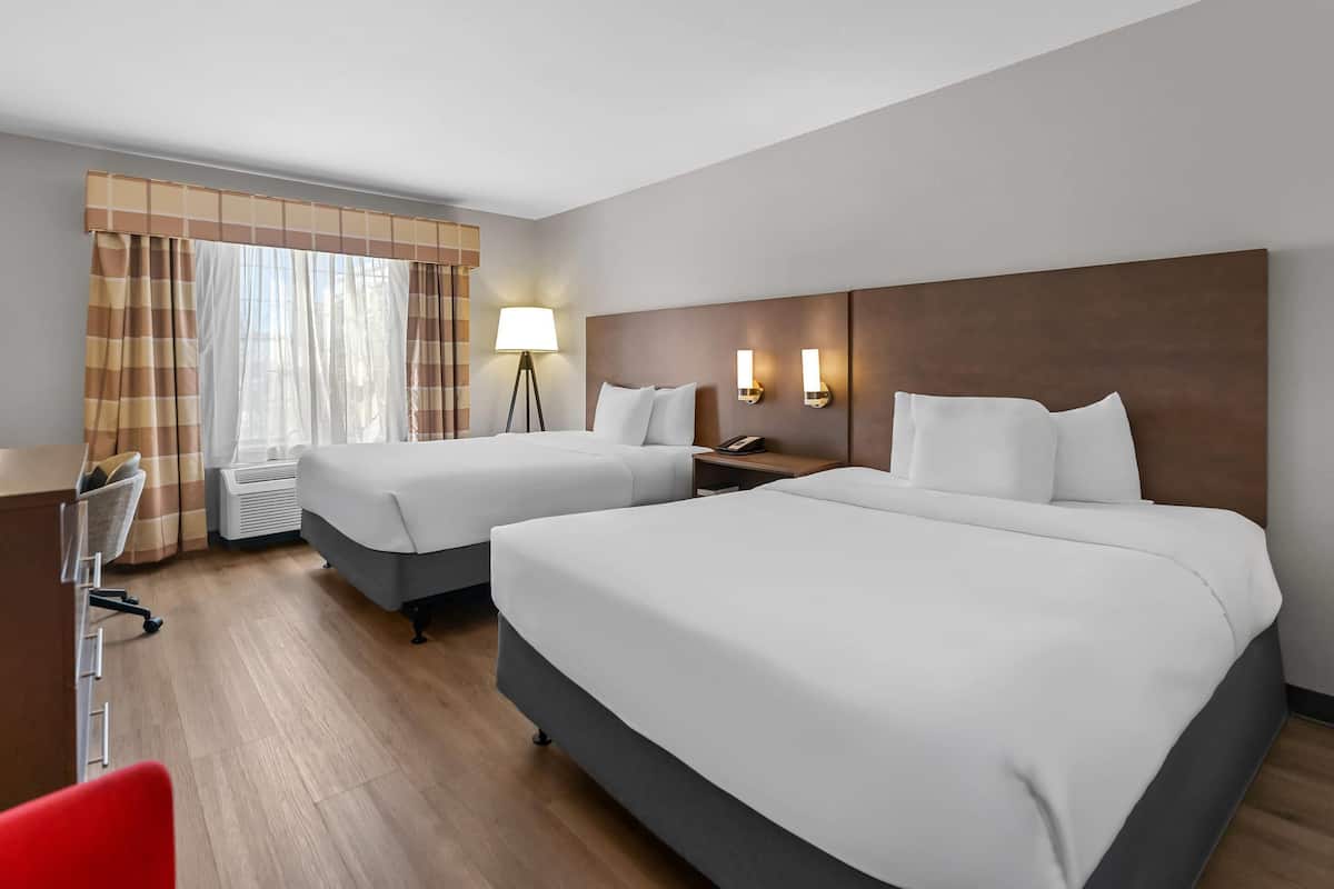A hotel room with two beds, a desk, a chair, a lamp, and a window with curtains.