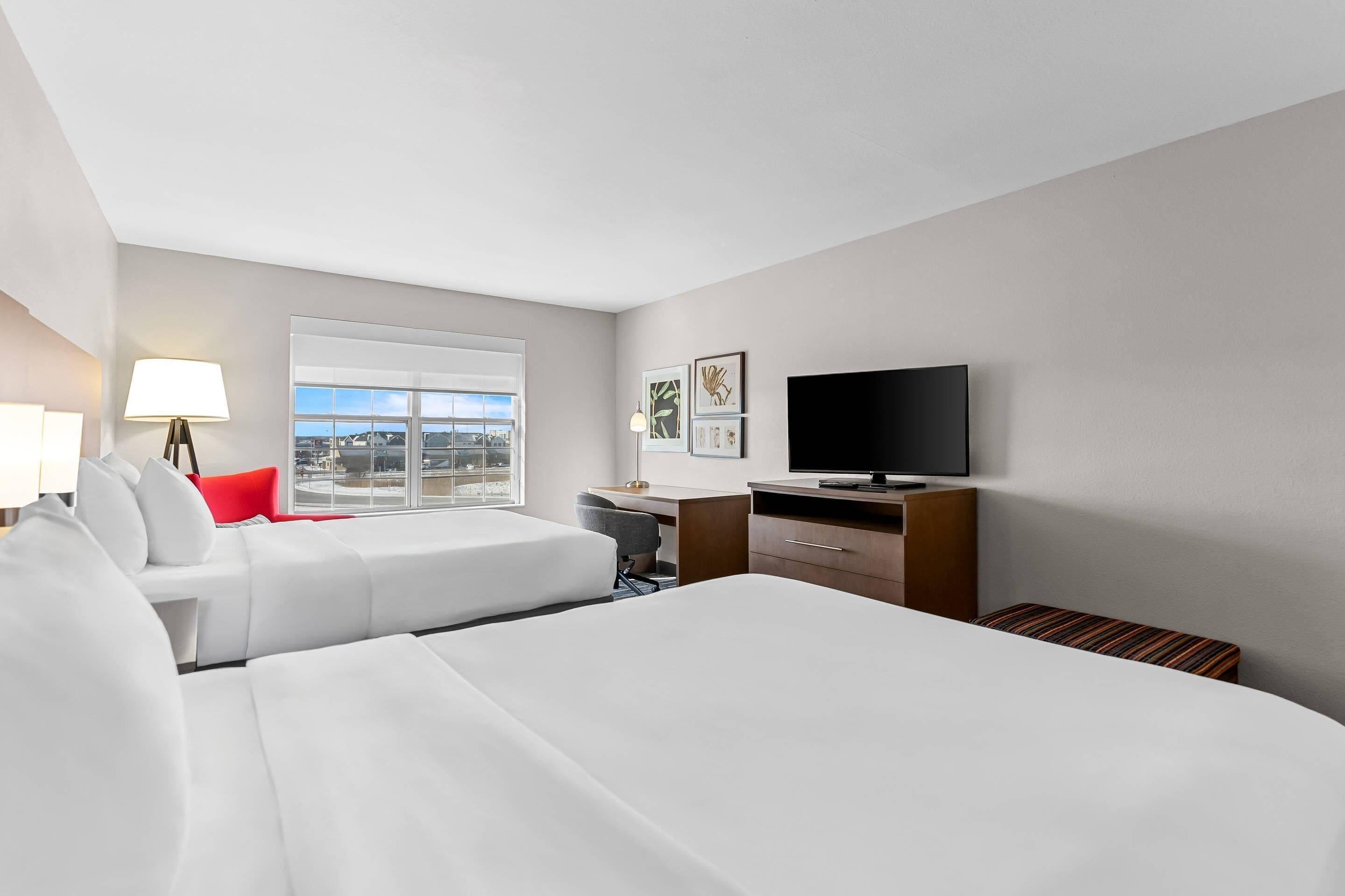 Een hotelkamer met twee bedden, een bureau, een televisie en een raam met uitzicht op de stad.