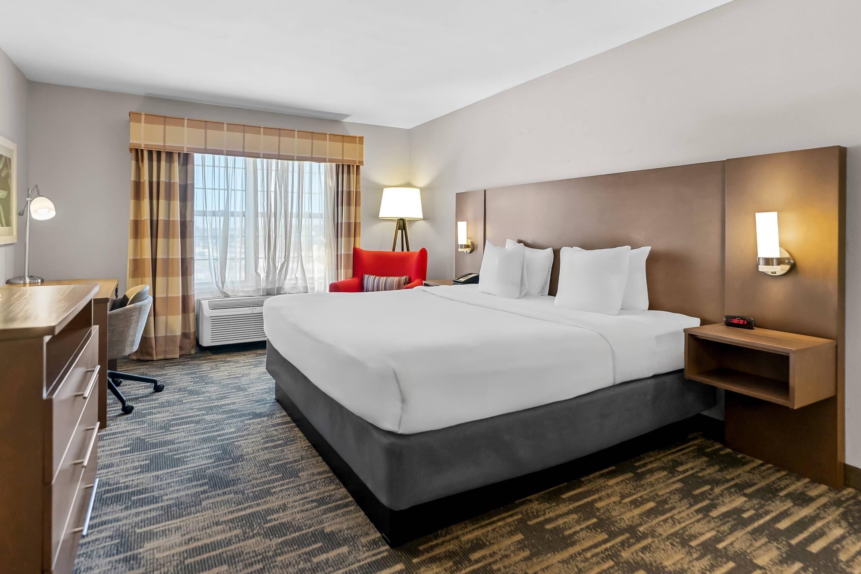 A hotel room with a large bed, a desk, a chair, a lamp, and a nightstand.