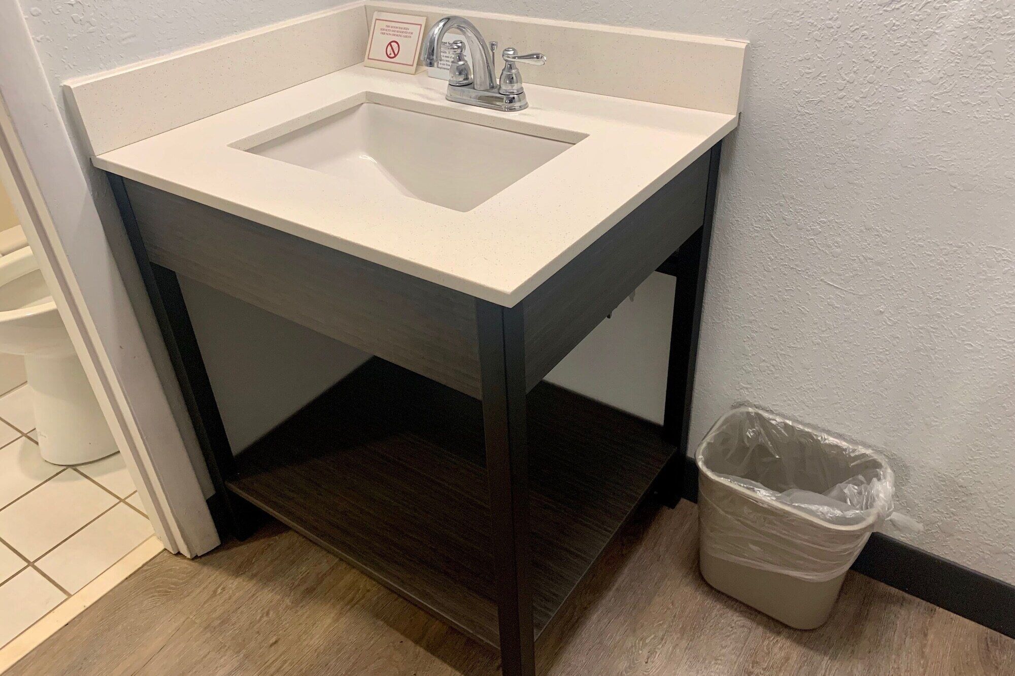 A bathroom sink with a mirror, a trash bin, and a towel rack.