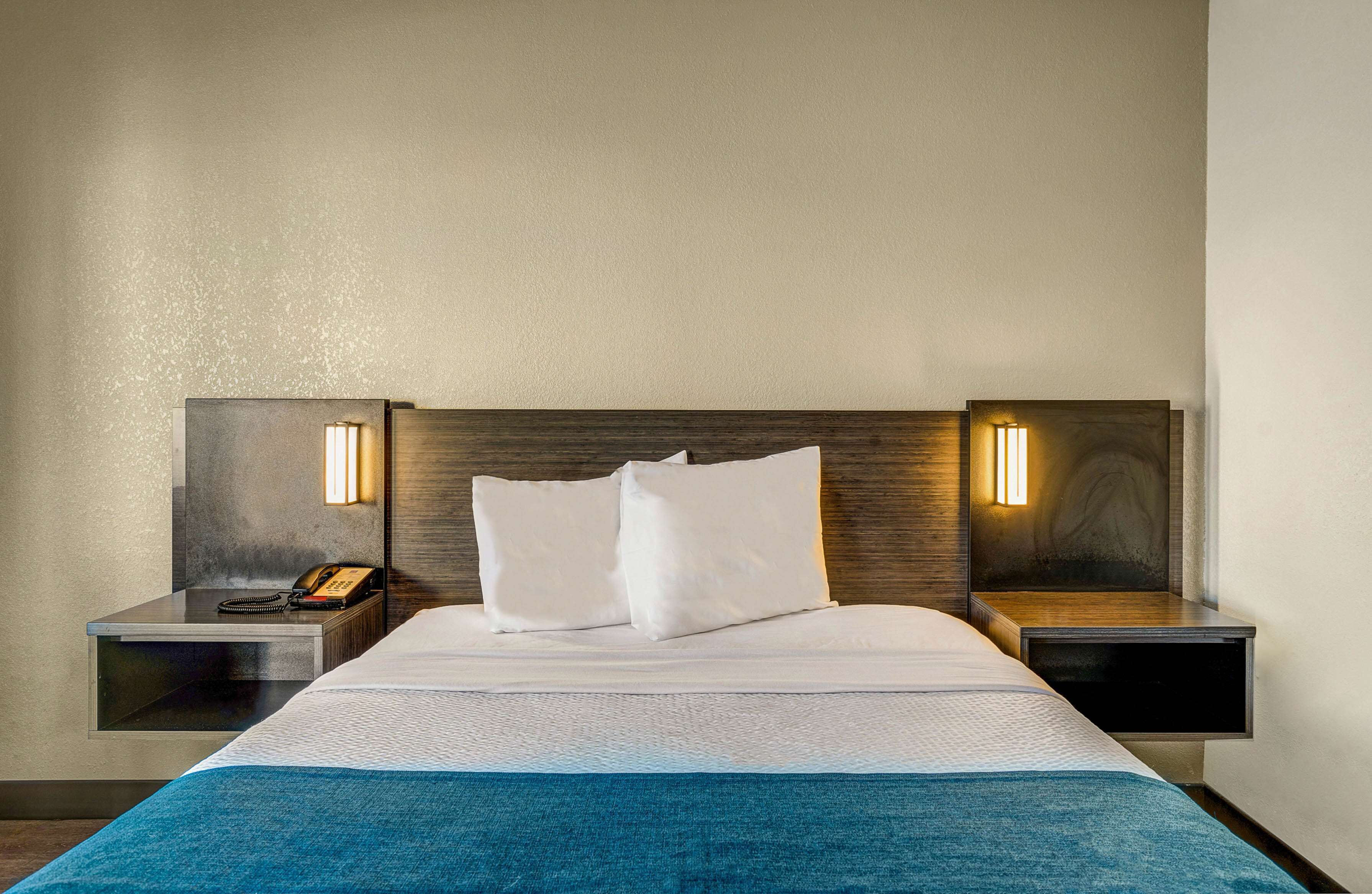 A hotel room with a large bed, two bedside tables, a telephone, and wall-mounted lamps.