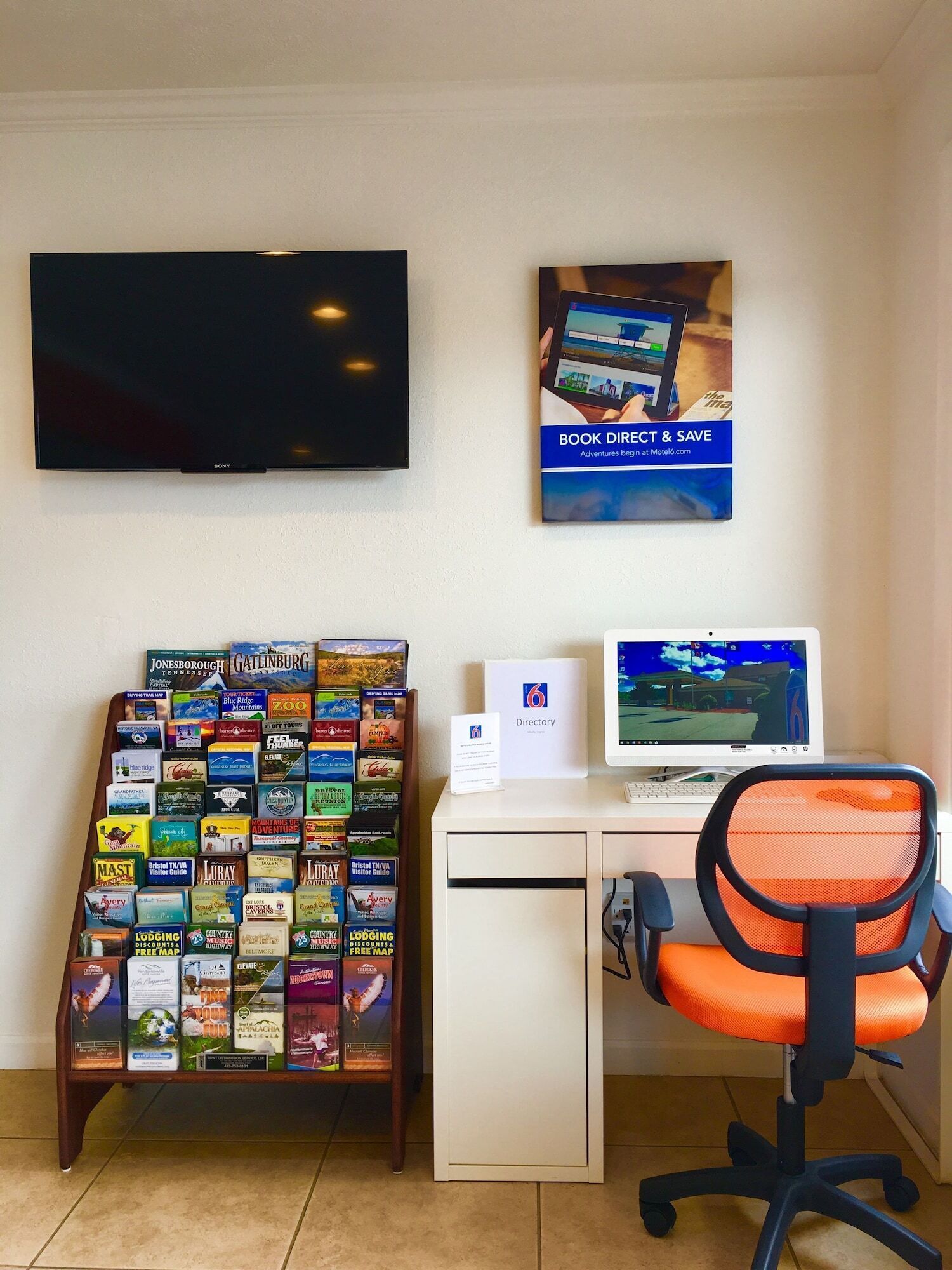 A hotel room with a desk, a computer, a TV, a directory, and a brochure rack.