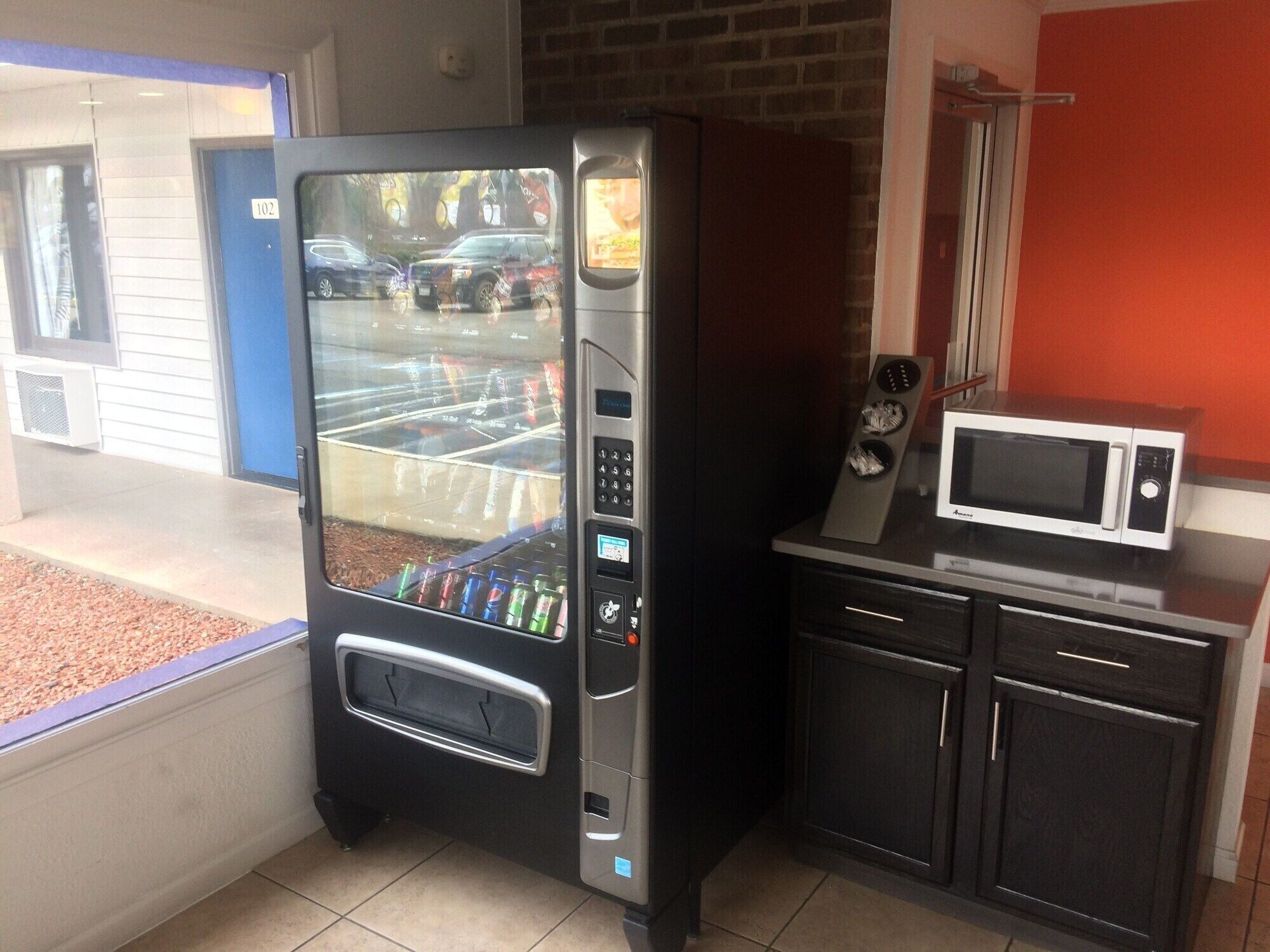 A vending machine with a glass door, a microwave, and a small kitchen area with cabinets.
