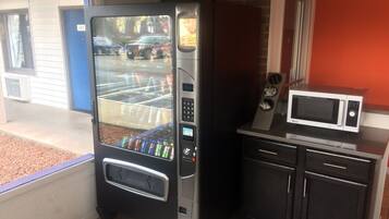A vending machine with a glass door, a microwave, and a small kitchen area with cabinets.