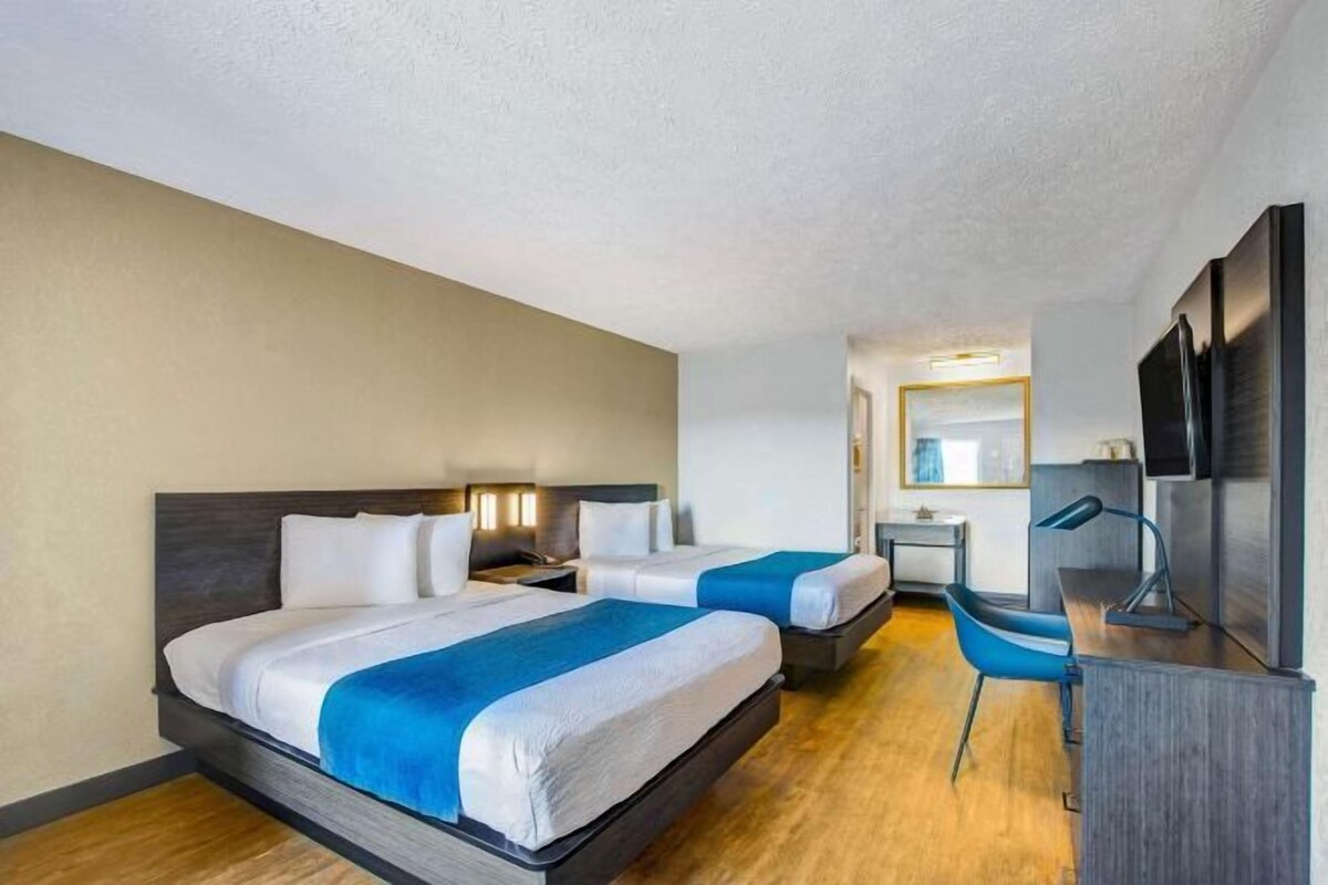 Ein Hotelzimmer mit zwei Betten, einem Schreibtisch, einem Stuhl und einem Fernseher.