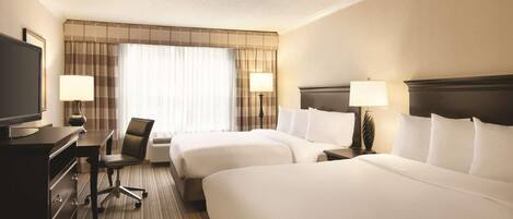 A hotel room with two beds, a desk with a chair, a television, and two lamps.